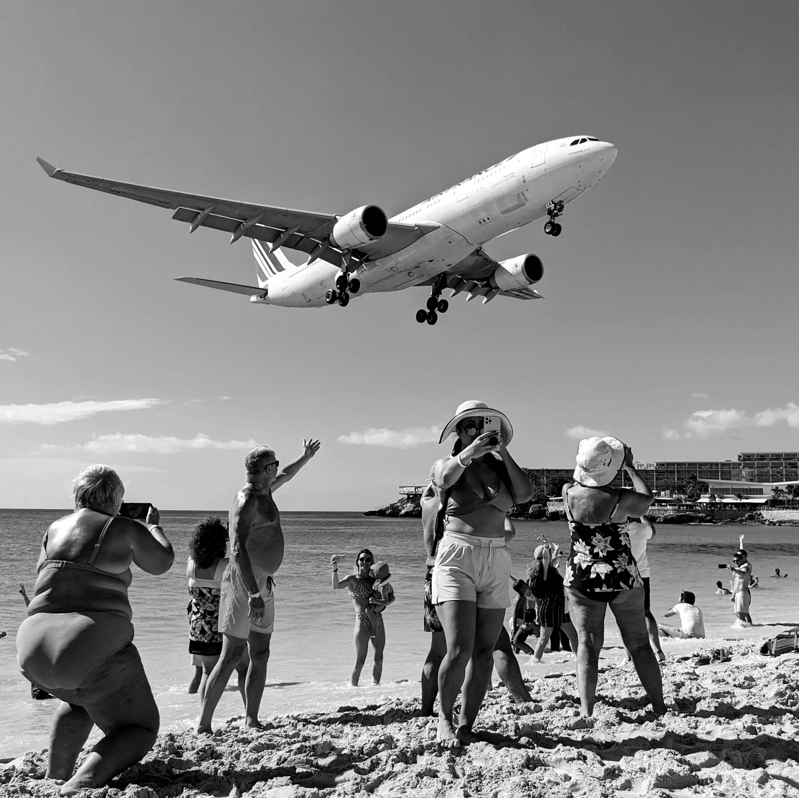 Black-and-white photo of an airliner on final approach passing low over a crowd on Maho Beach, Sint Maarten